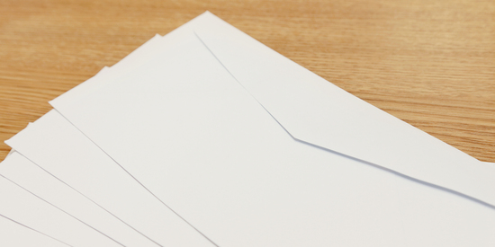 Stapel weißer Umschläge auf einer Holzoberfläche. Angeschnittene Ecken sind sichtbar.