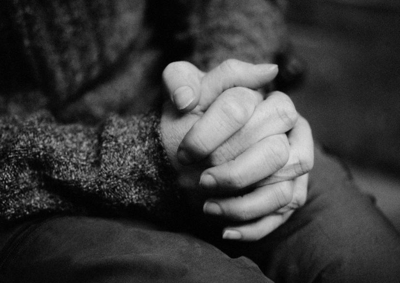 Nahaufnahme von zwei Händen, die ineinander verschränkt sind, vor einem unscharfen Hintergrund.