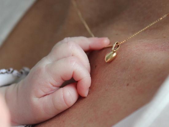 Babyhand greift sanft nach einer goldenen Halskette mit Anhänger auf der Haut einer Person.